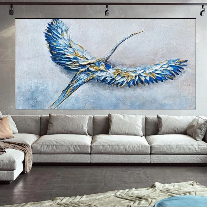 Large abstract painting of a bird with blue and gold feathers above a gray sofa.