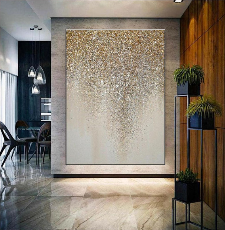 An abstract painting featuring golden glitter cascading in a drip-like pattern on a neutral beige canvas. A luxurious and elegant wall décor piece for modern interiors.