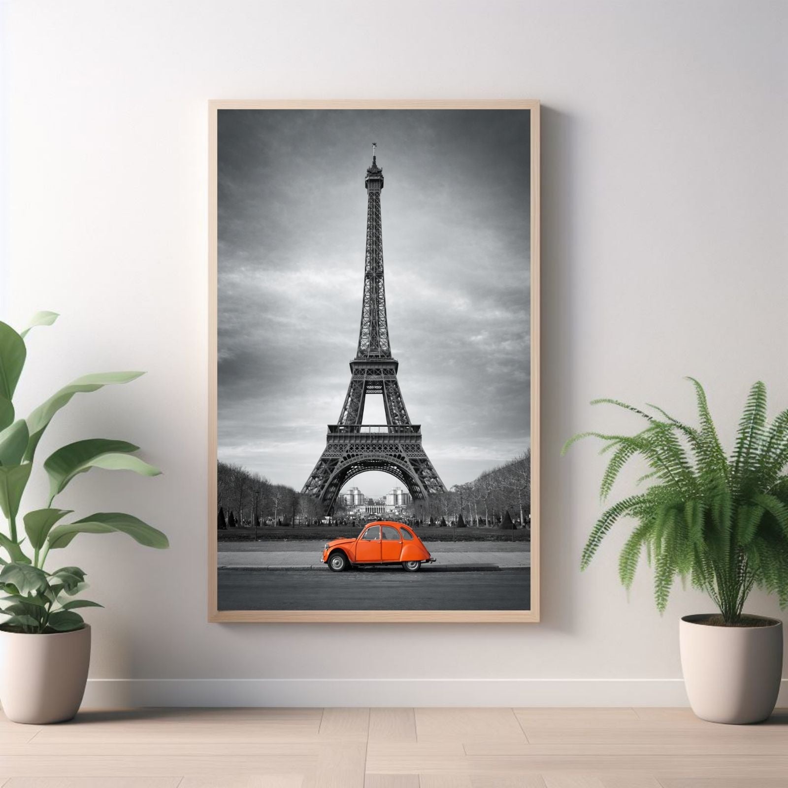 A selective color photograph of a bright orange vintage Citroen 2CV car parked in front of a black and white Eiffel Tower in Paris.